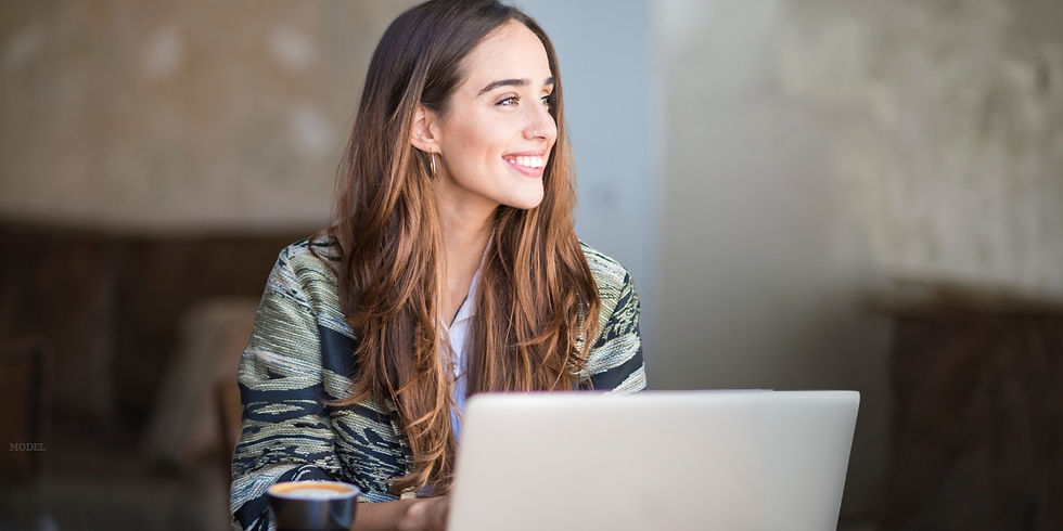 Woman with long brown hair sitting at a table with a laptop (model)